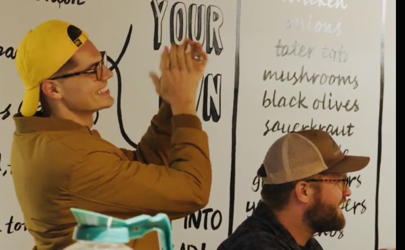 Two men are standing in front of a white board with the word your on it