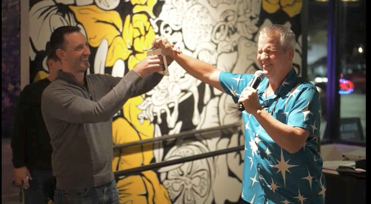 Two men toasting in front of a mural on the wall