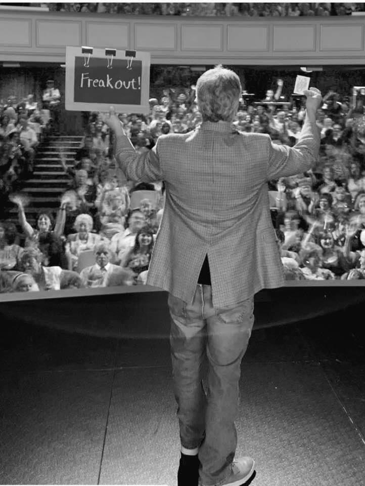 A man stands on a stage holding a sign that says freakout