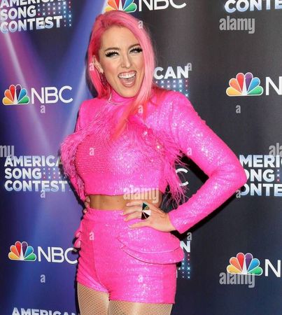 A woman with pink hair is standing in front of a nbc sign.