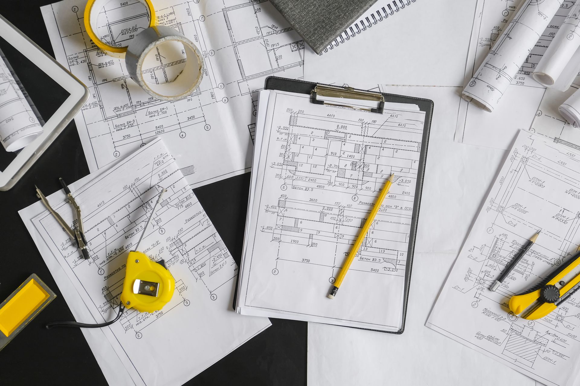 Des papiers, des outils et une tablette sur une surface de travail, suggérant des plans d'architecture ou de design en cours d'élaboration.