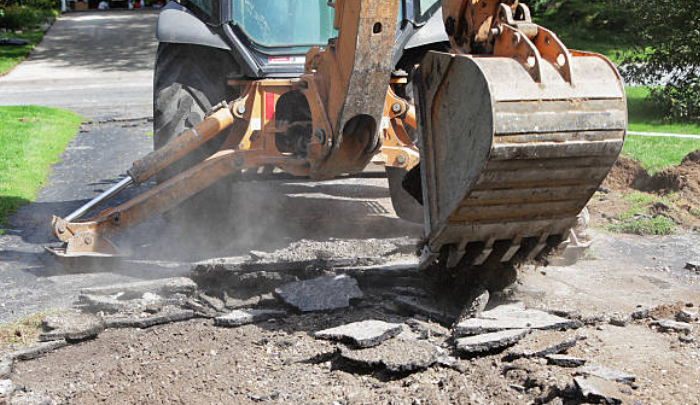 Three construction workers use shovels and a rake to spread fresh asphalt in front of a residential home.