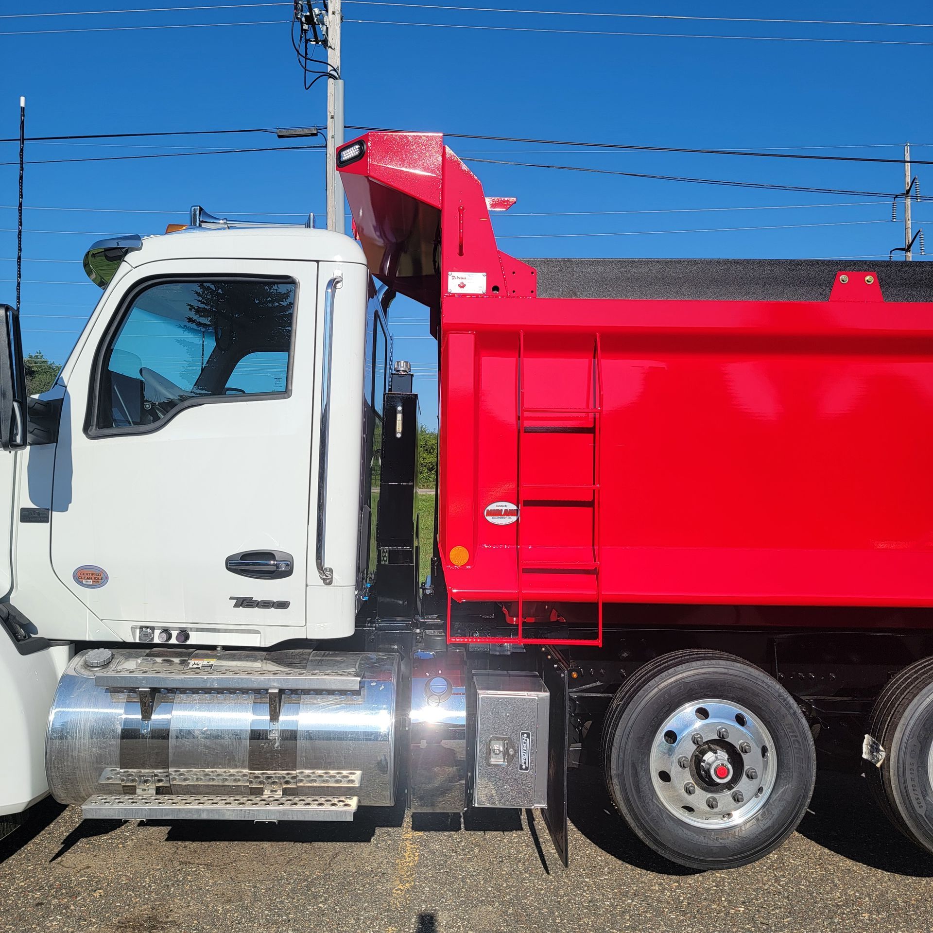 A red dump truck is parked next to a white truck