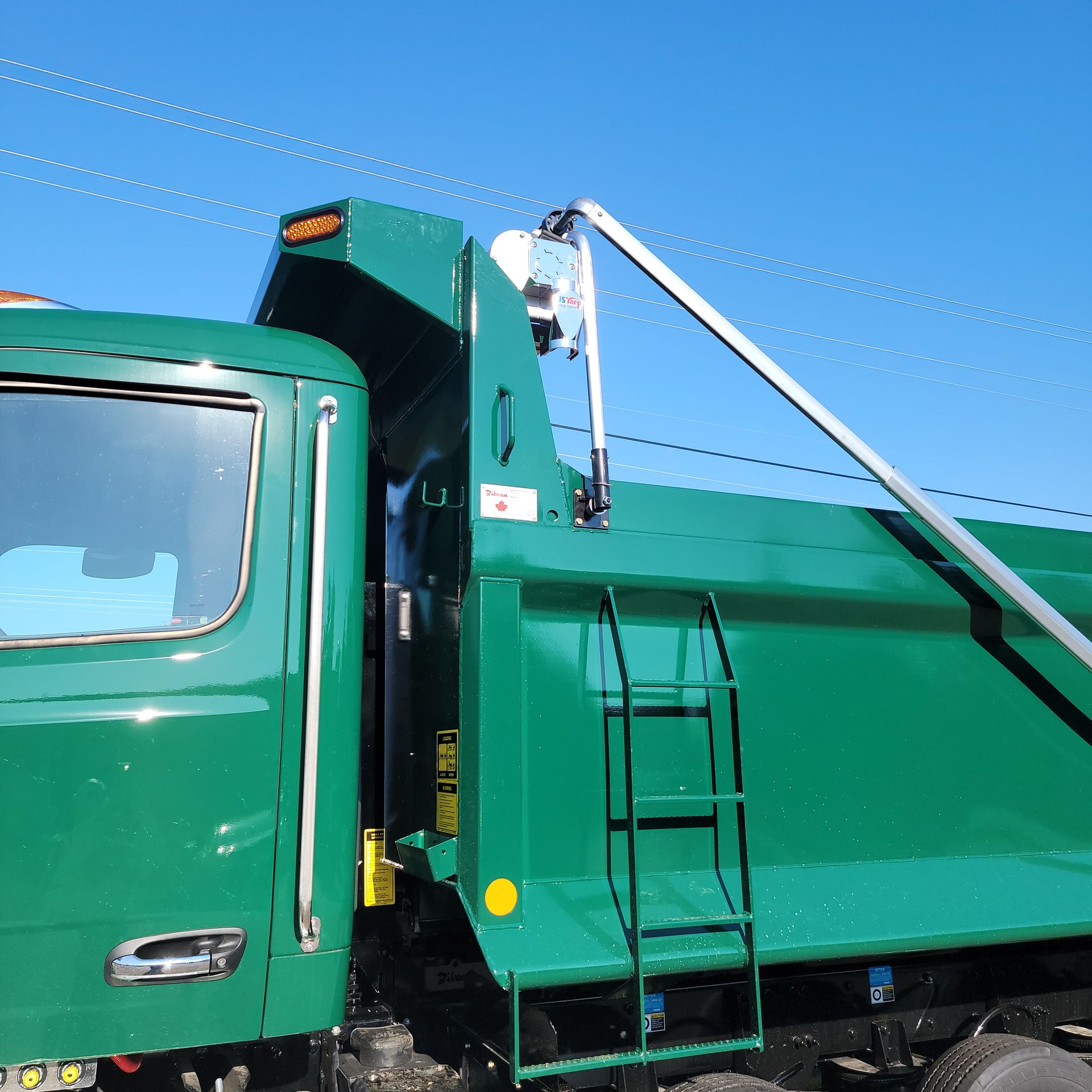 A green dump truck with a ladder attached to it