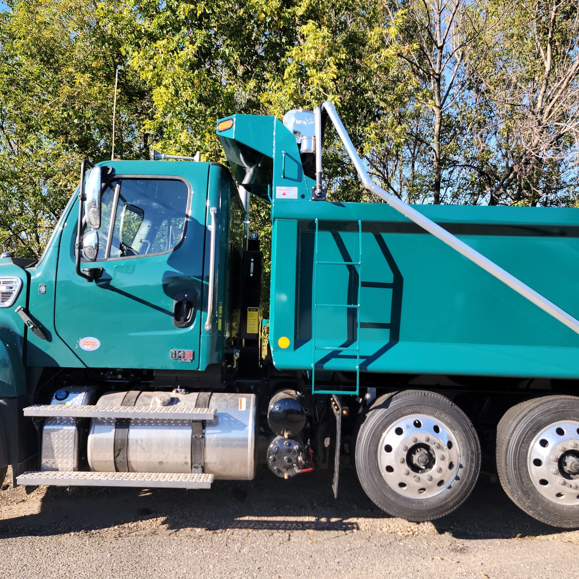 A green dump truck is parked on the side of the road