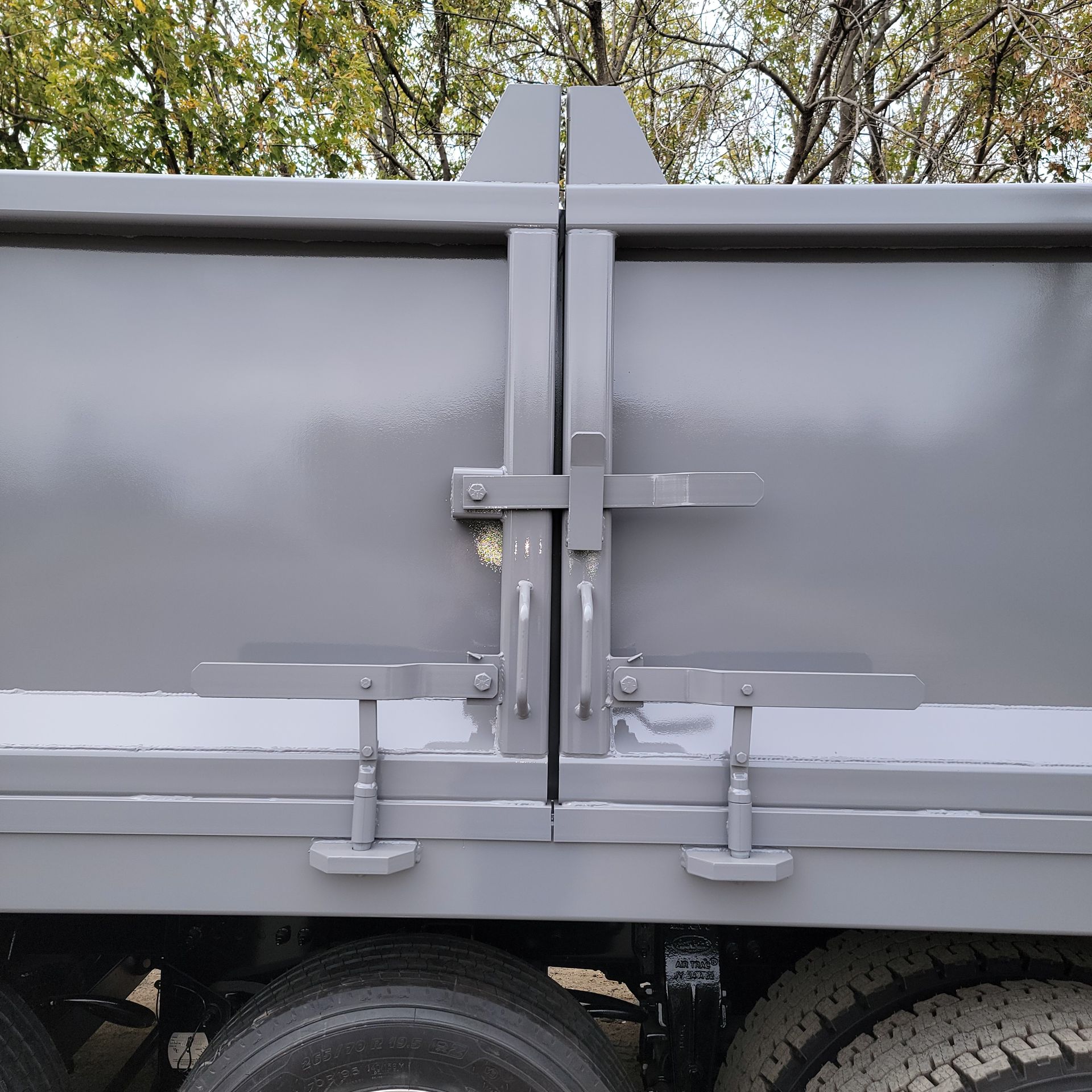 A gray dump truck is parked in a parking lot with trees in the background