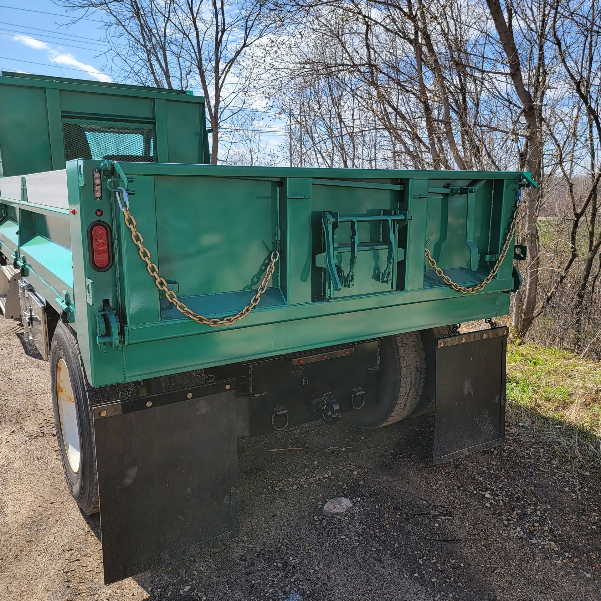 A green dump truck is parked on the side of the road.