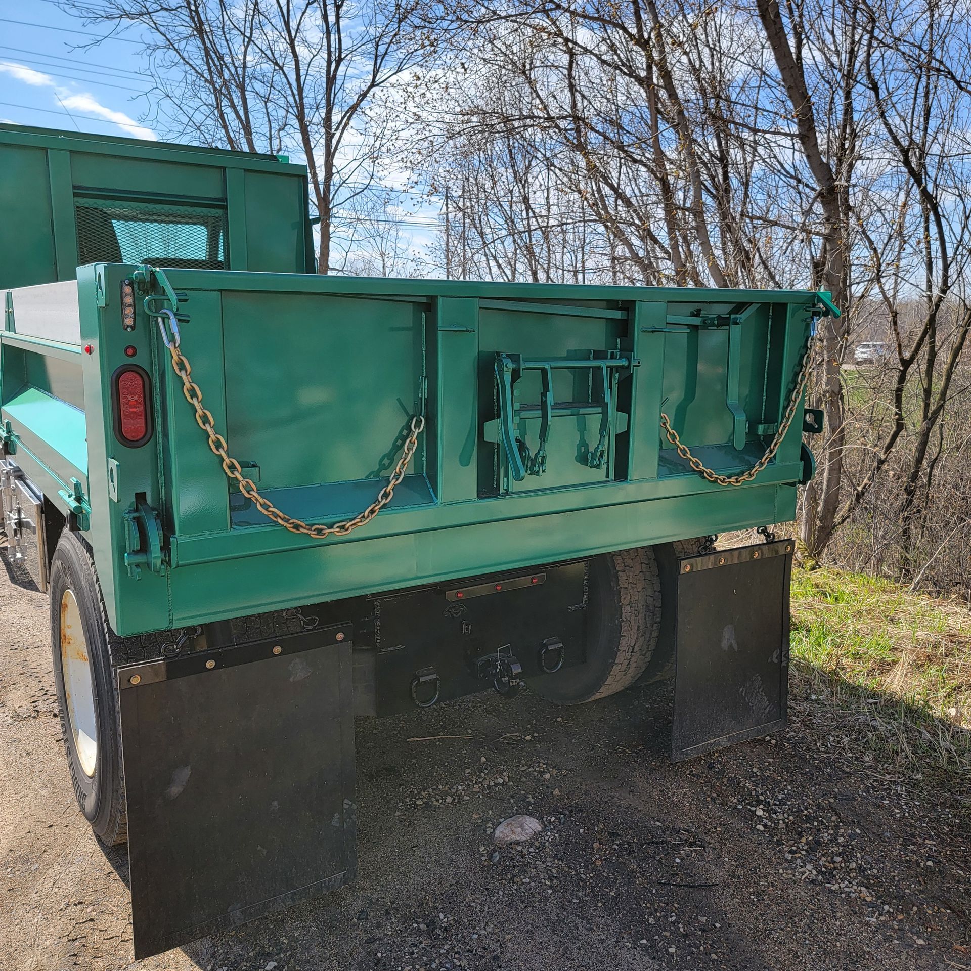 A green dump truck is parked on the side of a dirt road.