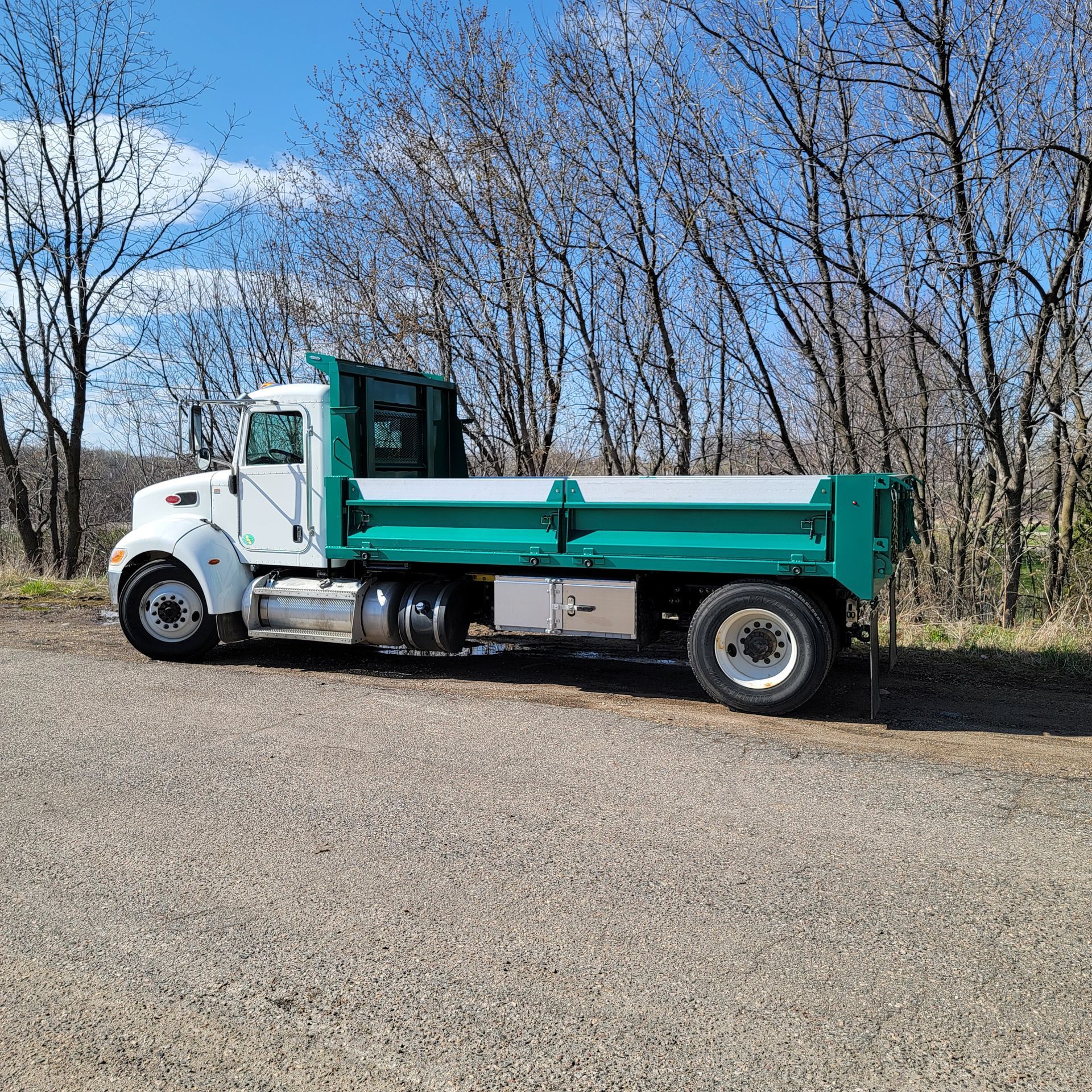A white and green dump truck is parked in a gravel lot.