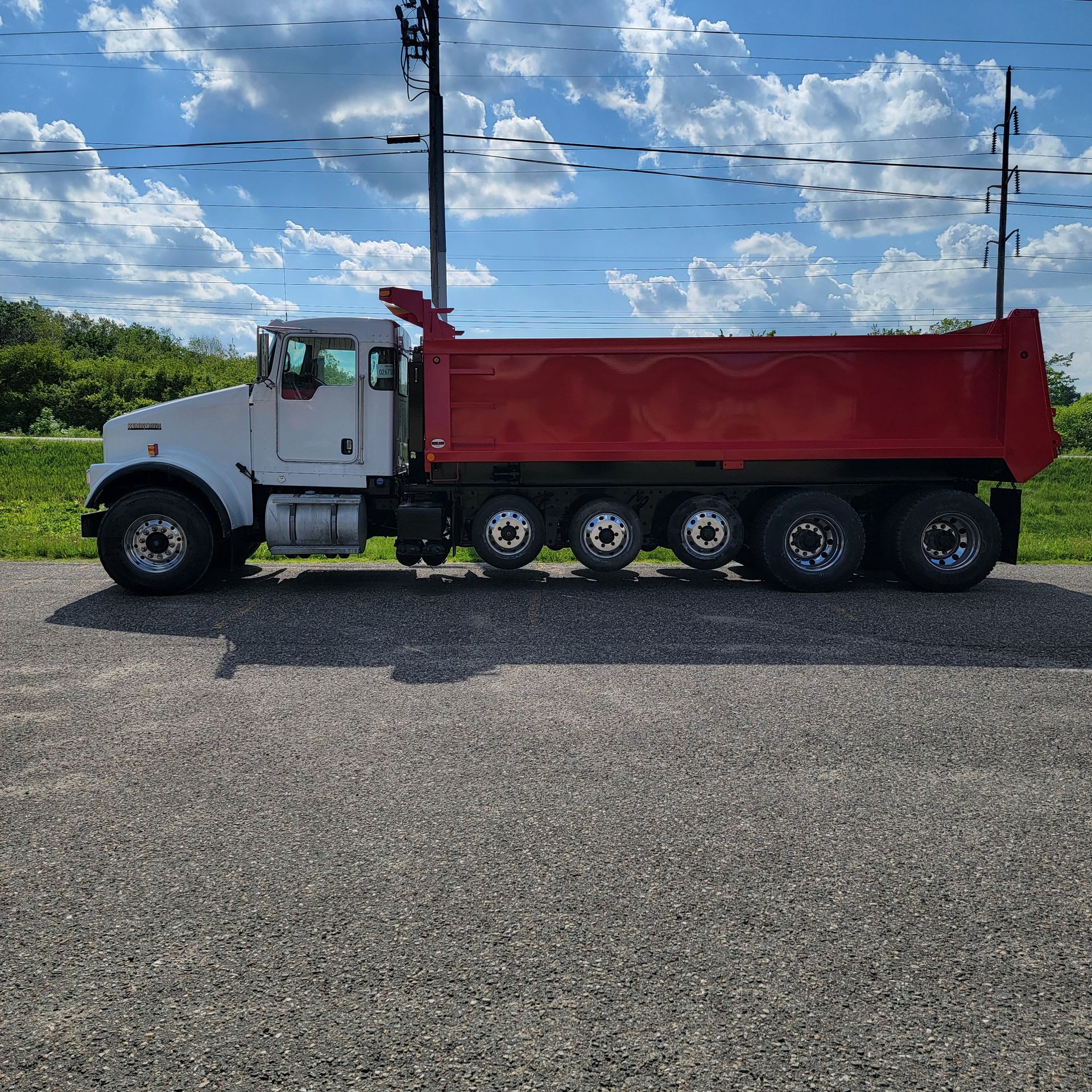 A white dump truck with a red bed is parked in a gravel lot.
