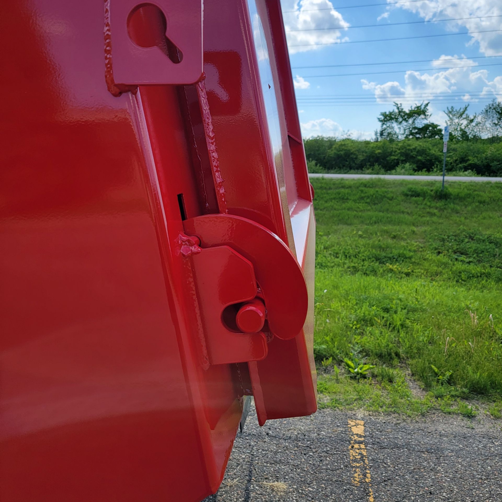 A red dumpster is parked on the side of the road next to a grassy field.