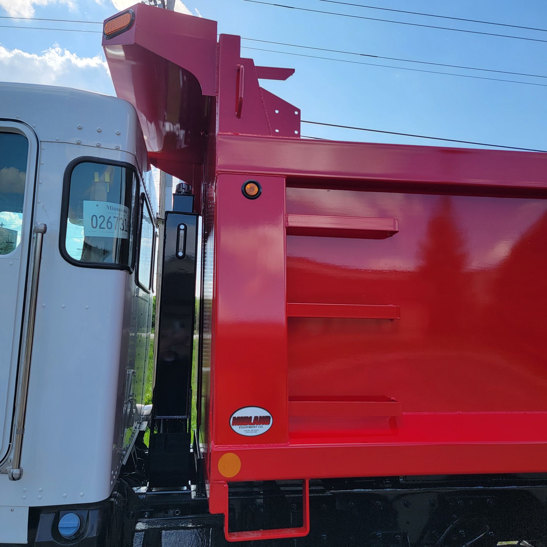 A red dump truck is parked next to a white truck