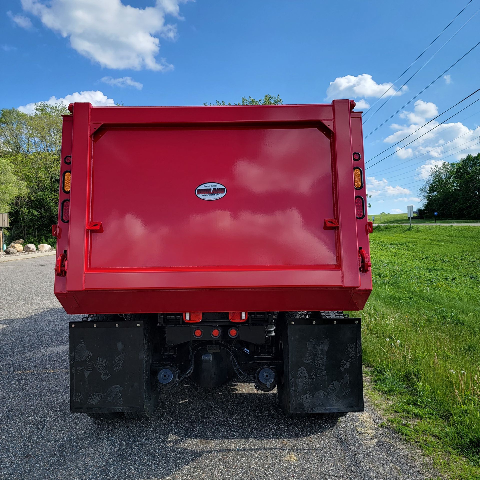A red dump truck is parked on the side of a gravel road.