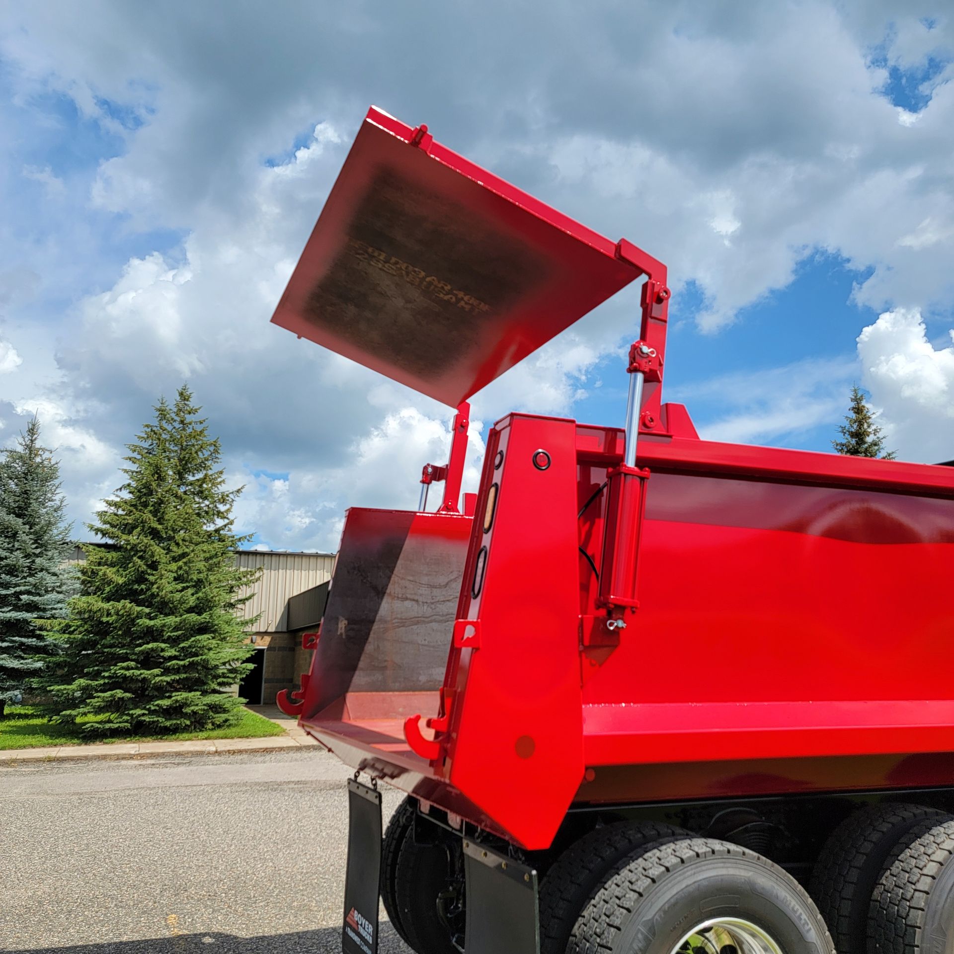 A red dump truck with the lid open is parked on the side of the road.
