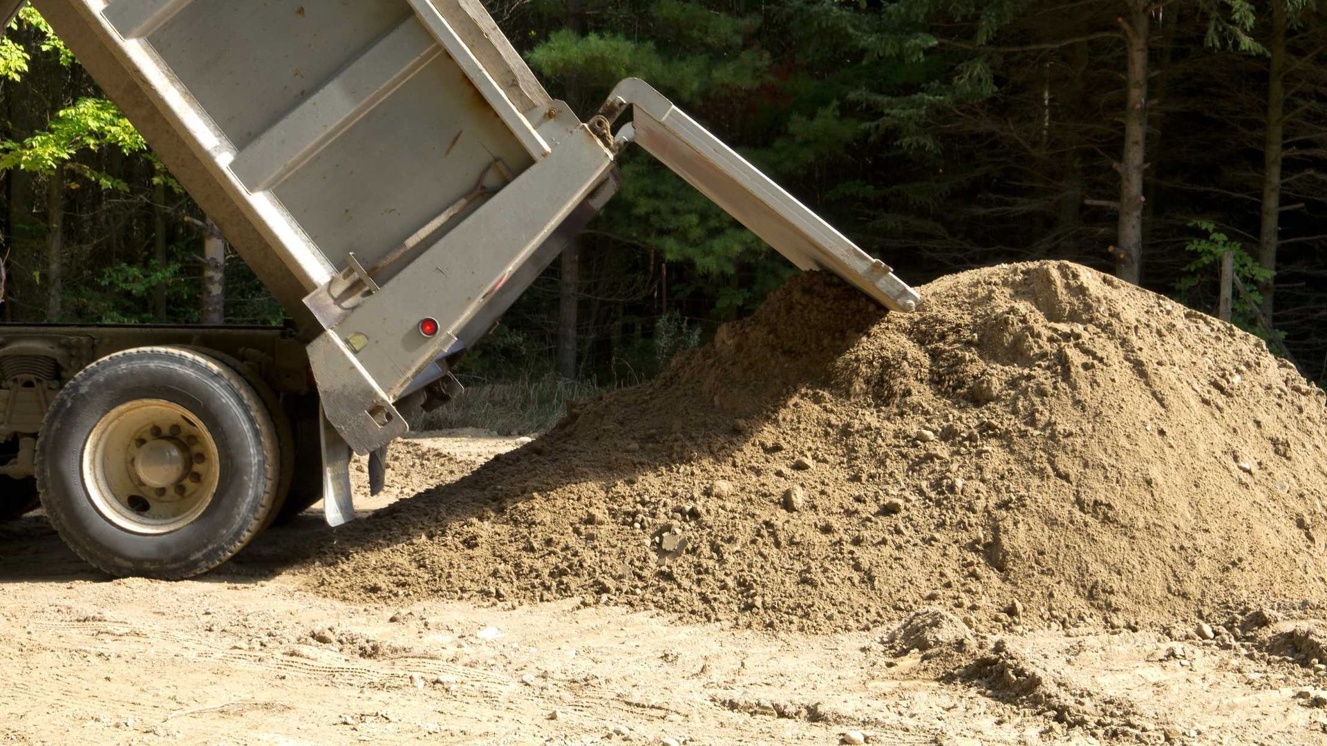 A dump truck is dumping a pile of dirt on a dirt road.