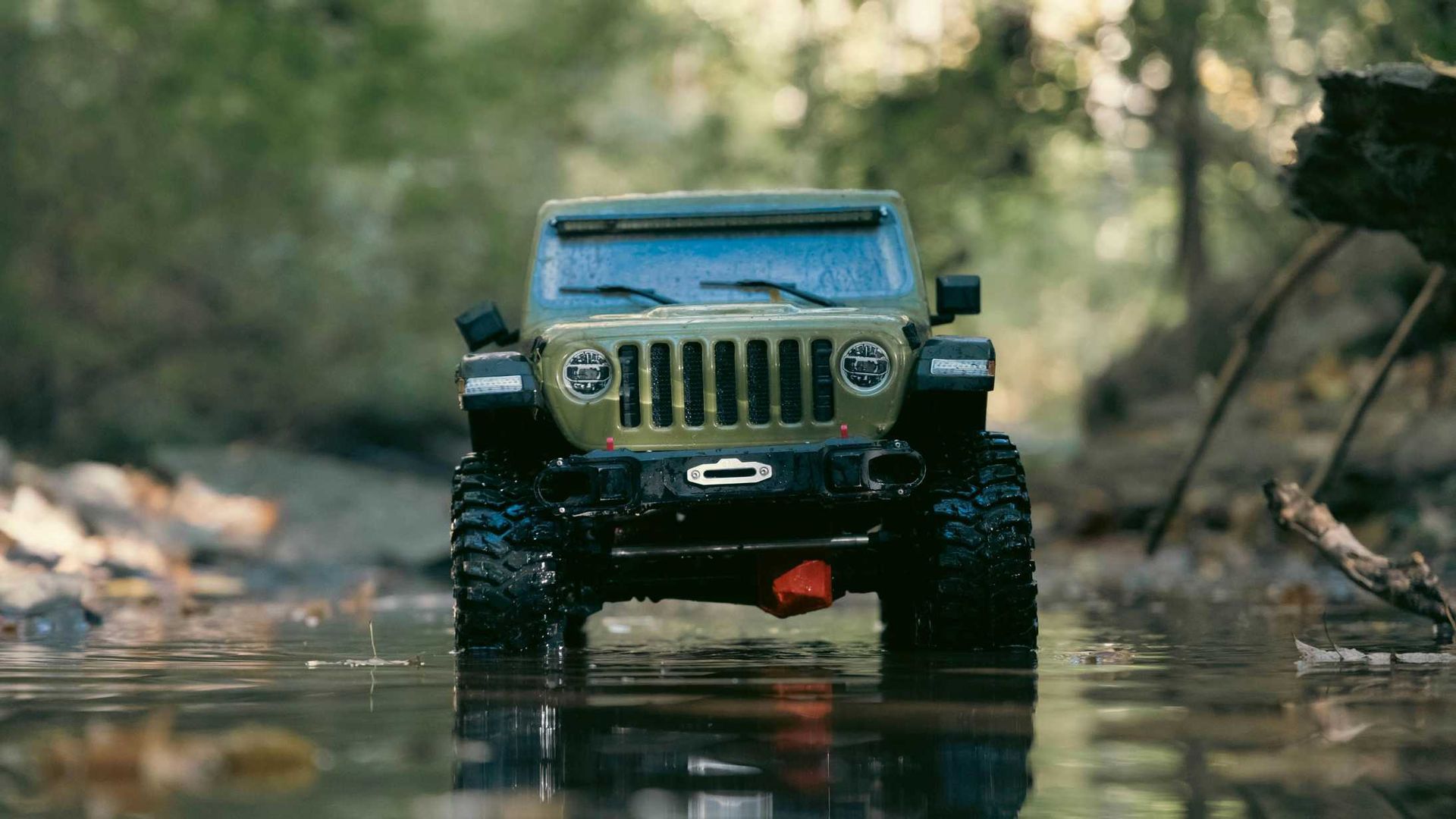 A toy jeep is driving through a stream in the woods.