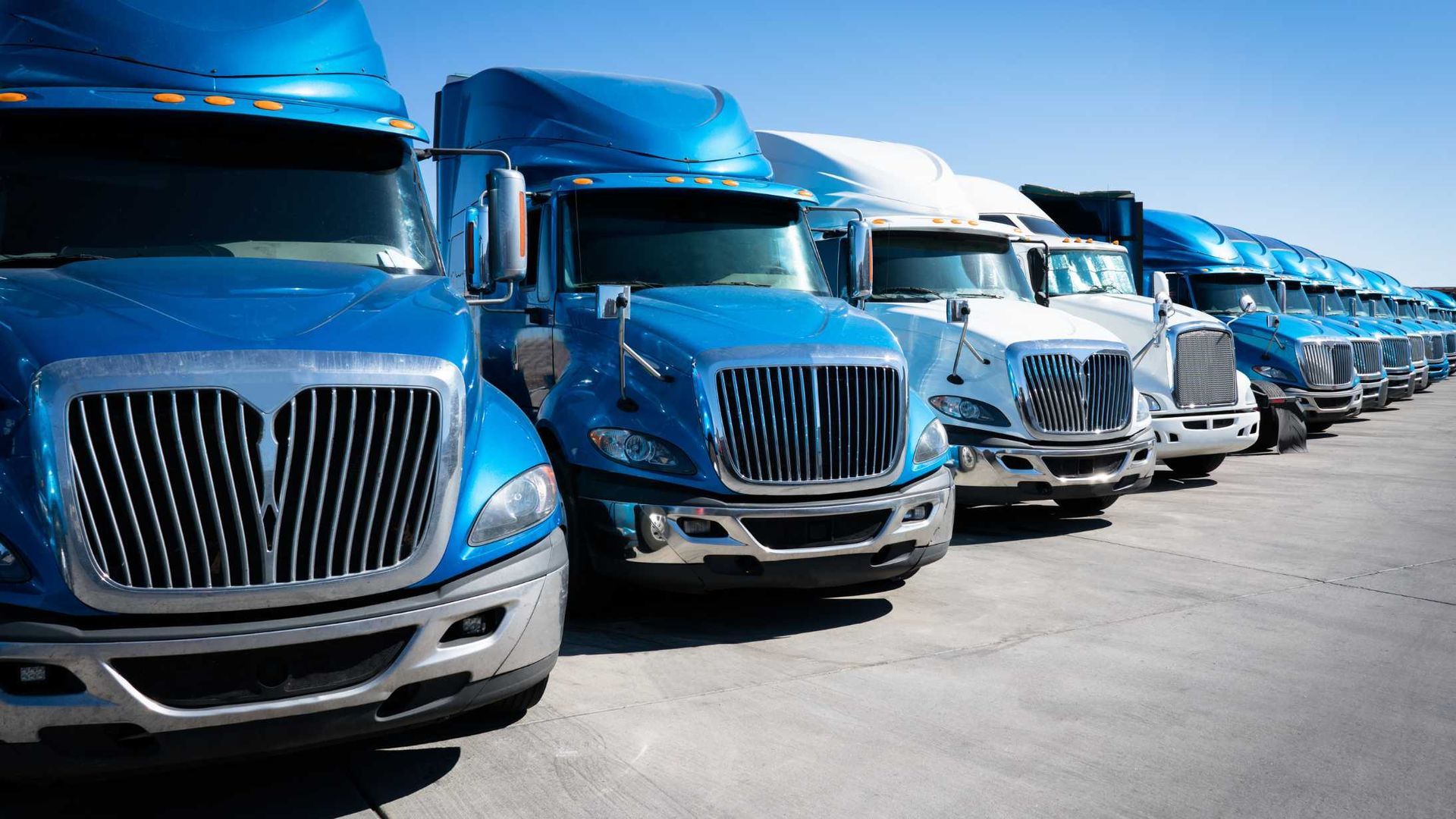 A row of blue semi trucks are parked in a parking lot.