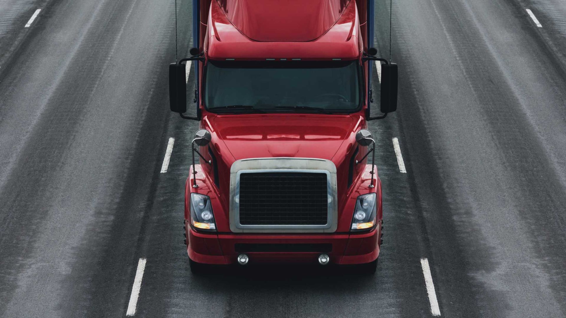 A red semi truck is driving down a wet highway.