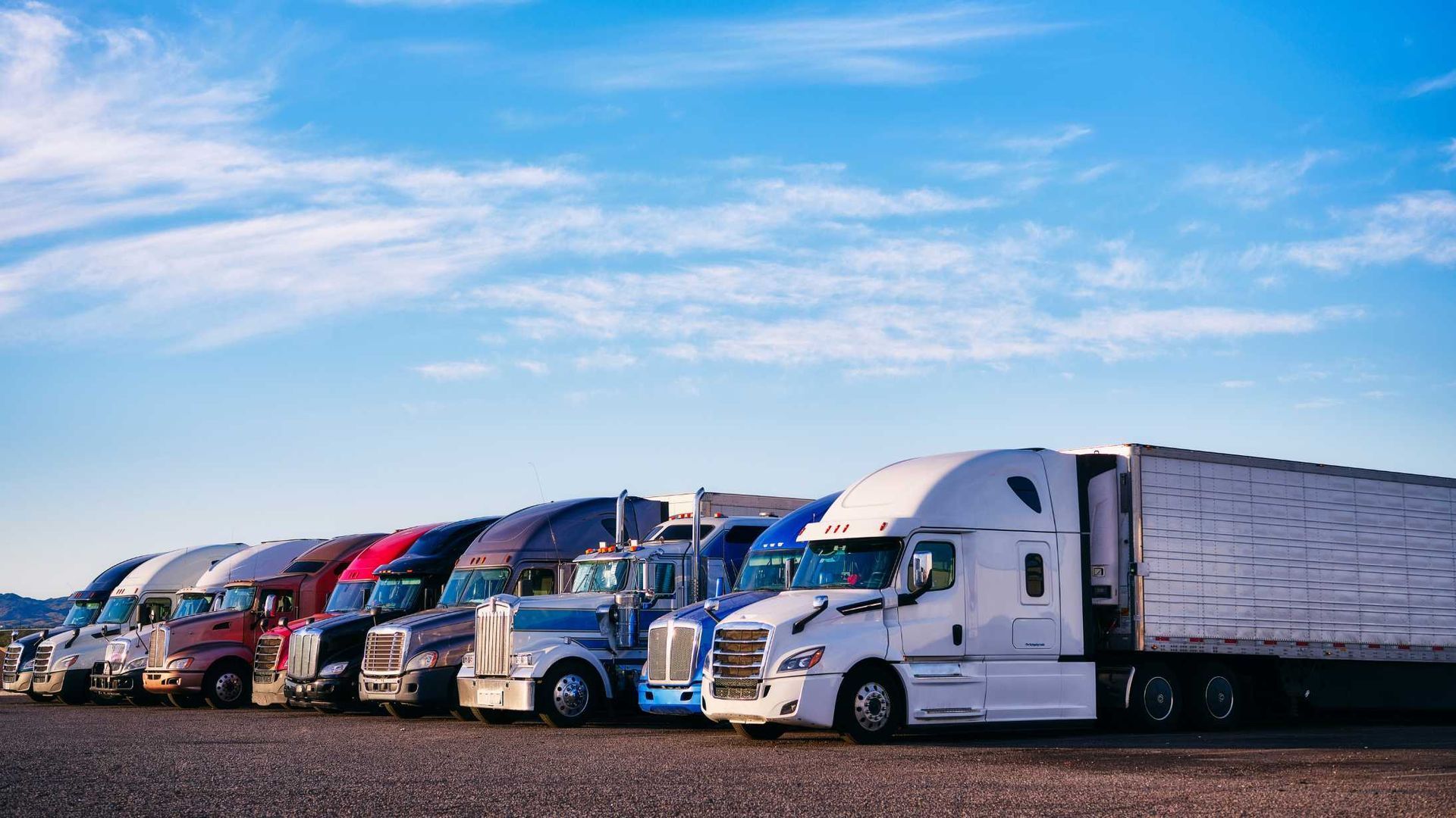 A row of semi trucks are parked in a parking lot.