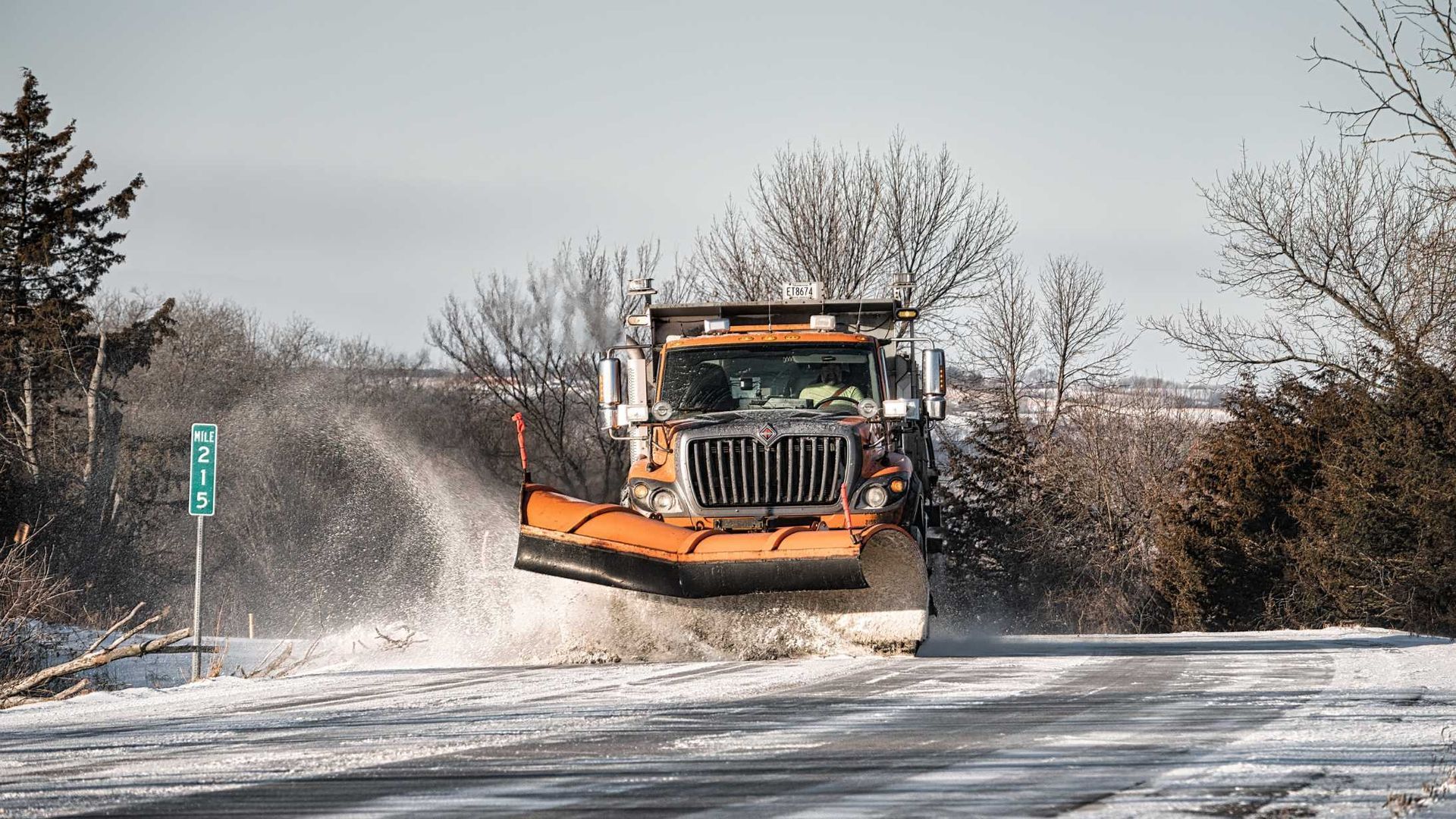A snow plow is driving down a snow covered road.