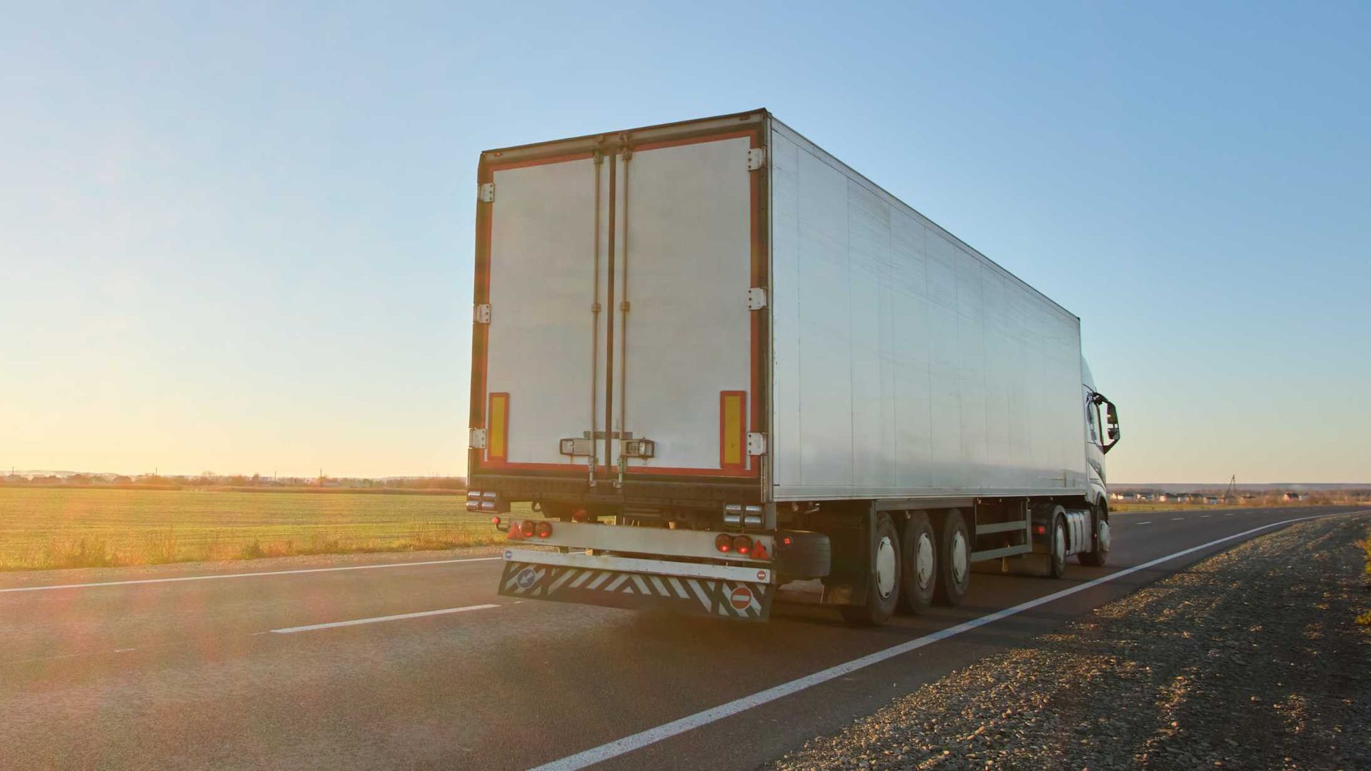 A semi truck is driving down a highway at sunset.