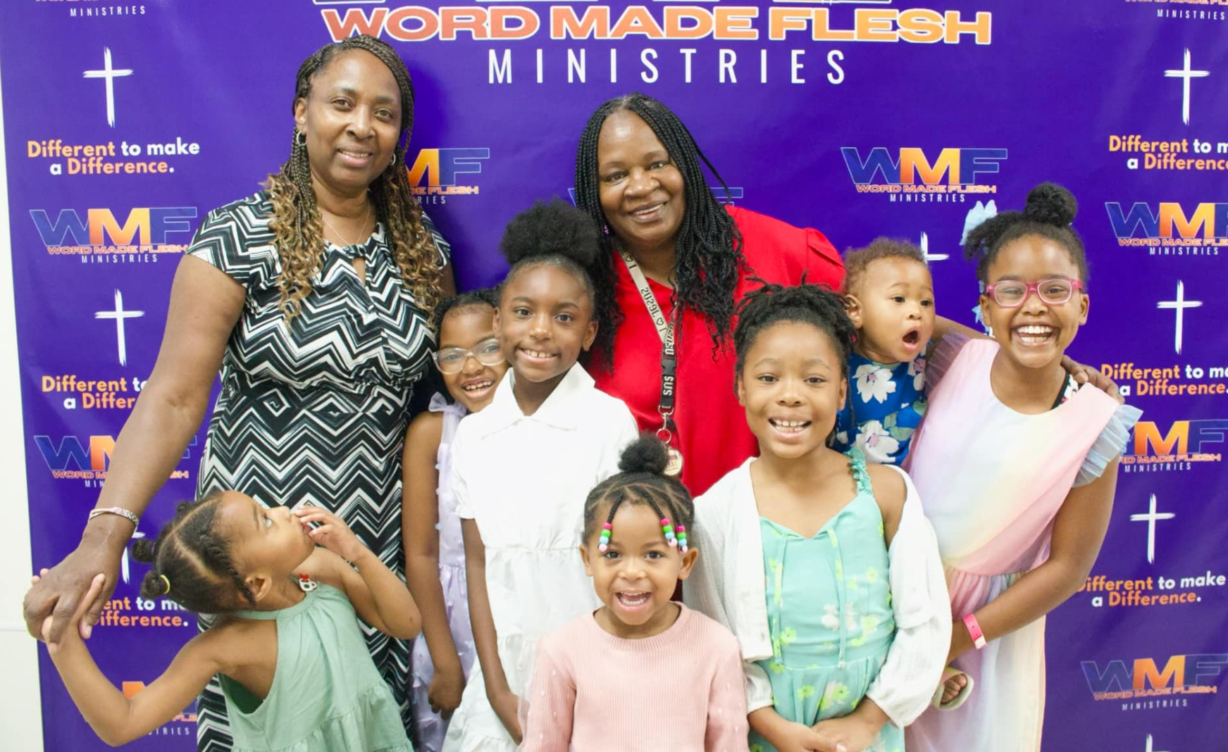 Two women and several children smile in front of a church banner.