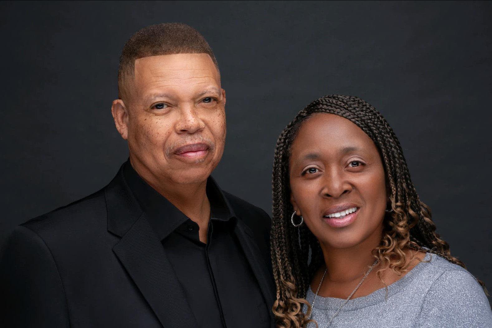 Man and woman in professional attire, smiling, posing together against a dark background.
