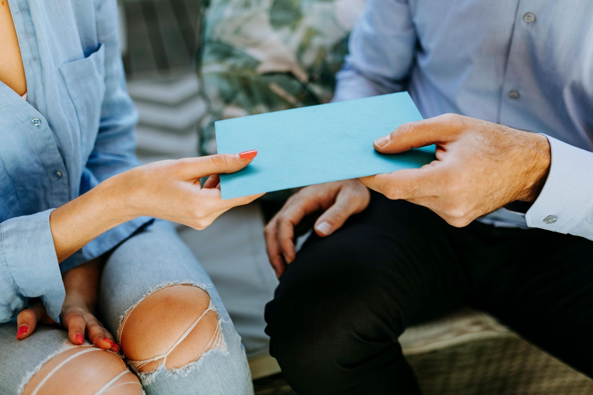 Woman and man hands exchanging a teal-colored card. Close-up. Outdoor setting.