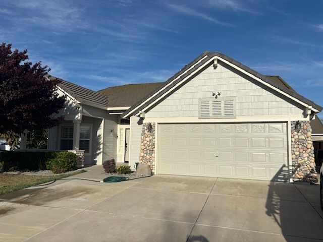 Yellow house with black roof, cluttered yard, plants, and blue sky.