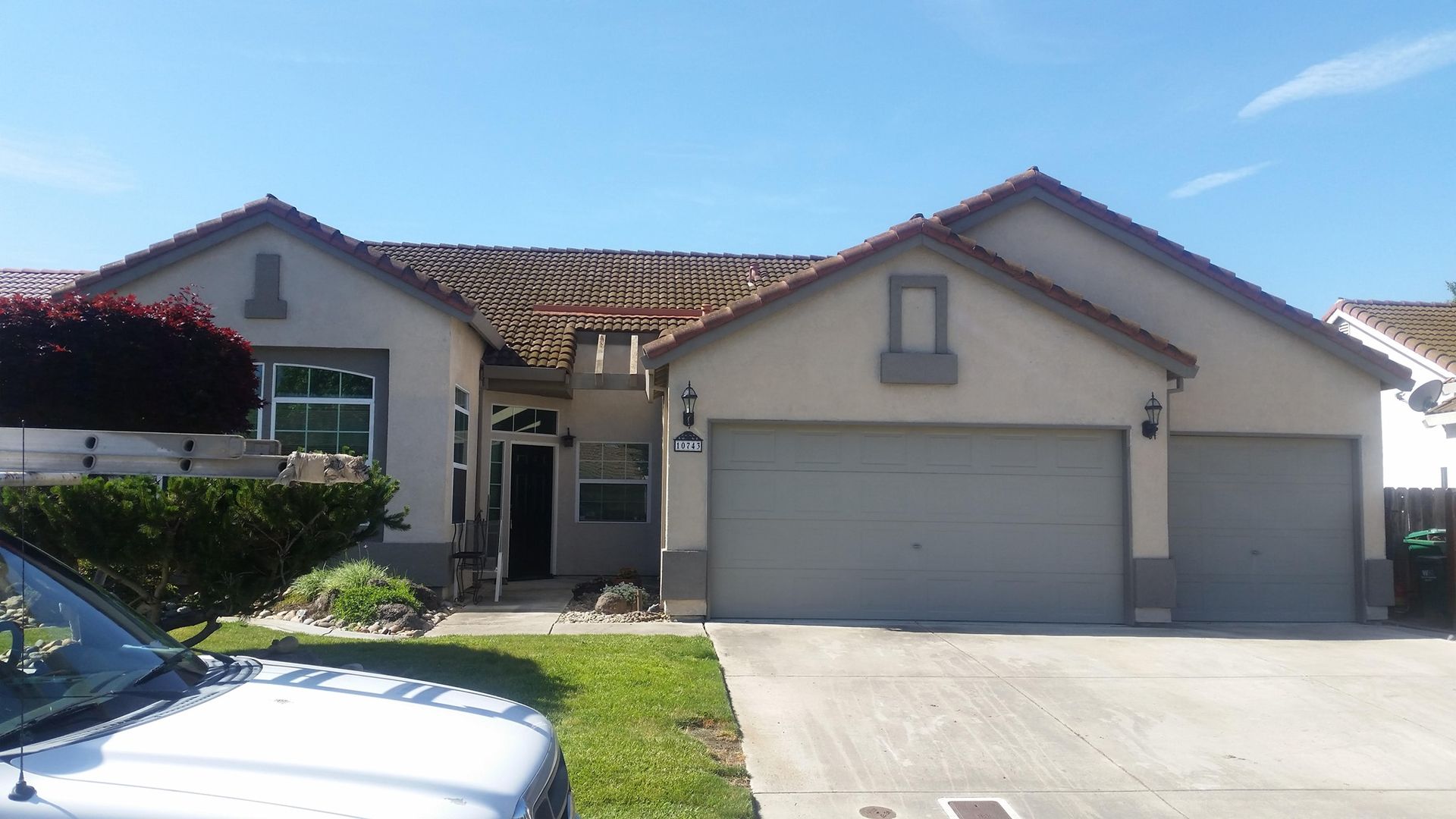 Tan stucco house with red tile roof, two-car garage, and green lawn. Bright, sunny day.