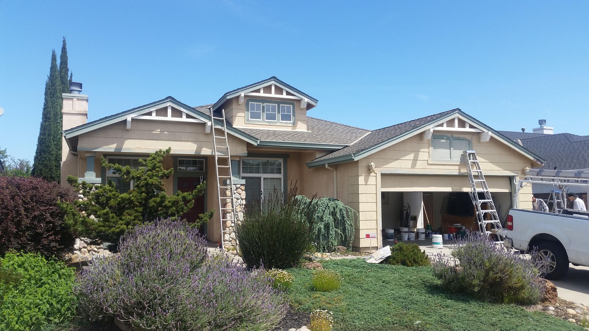 House being painted, beige stucco with white trim, ladder, and truck parked in front.
