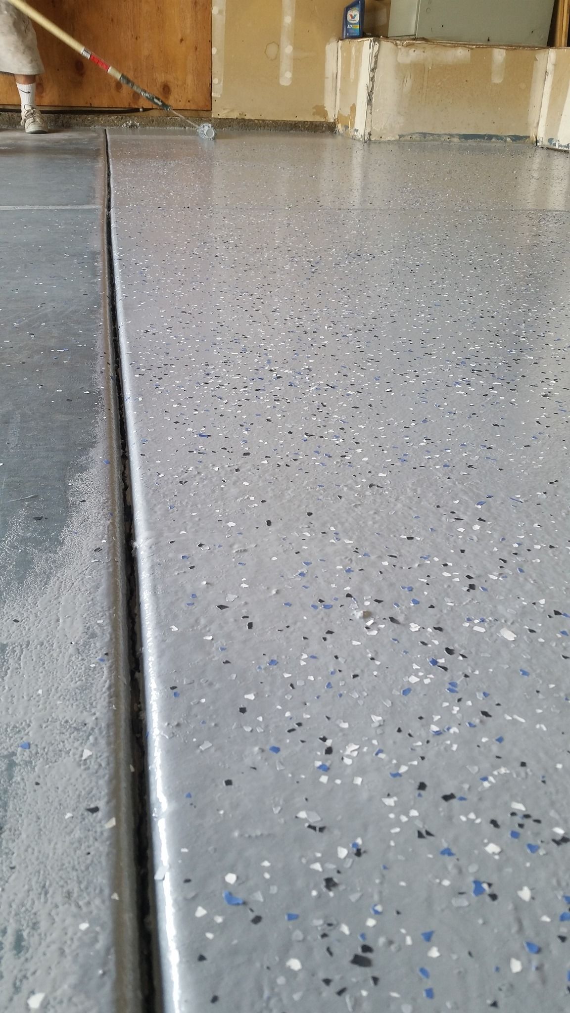 Garage floor with speckled epoxy coating being applied. Gray and white chips, with a black strip.