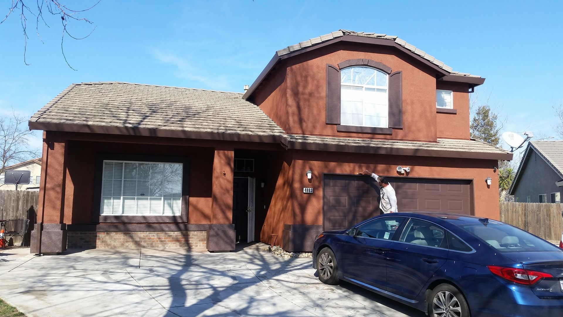 Brown stucco house with a blue car parked in the driveway.