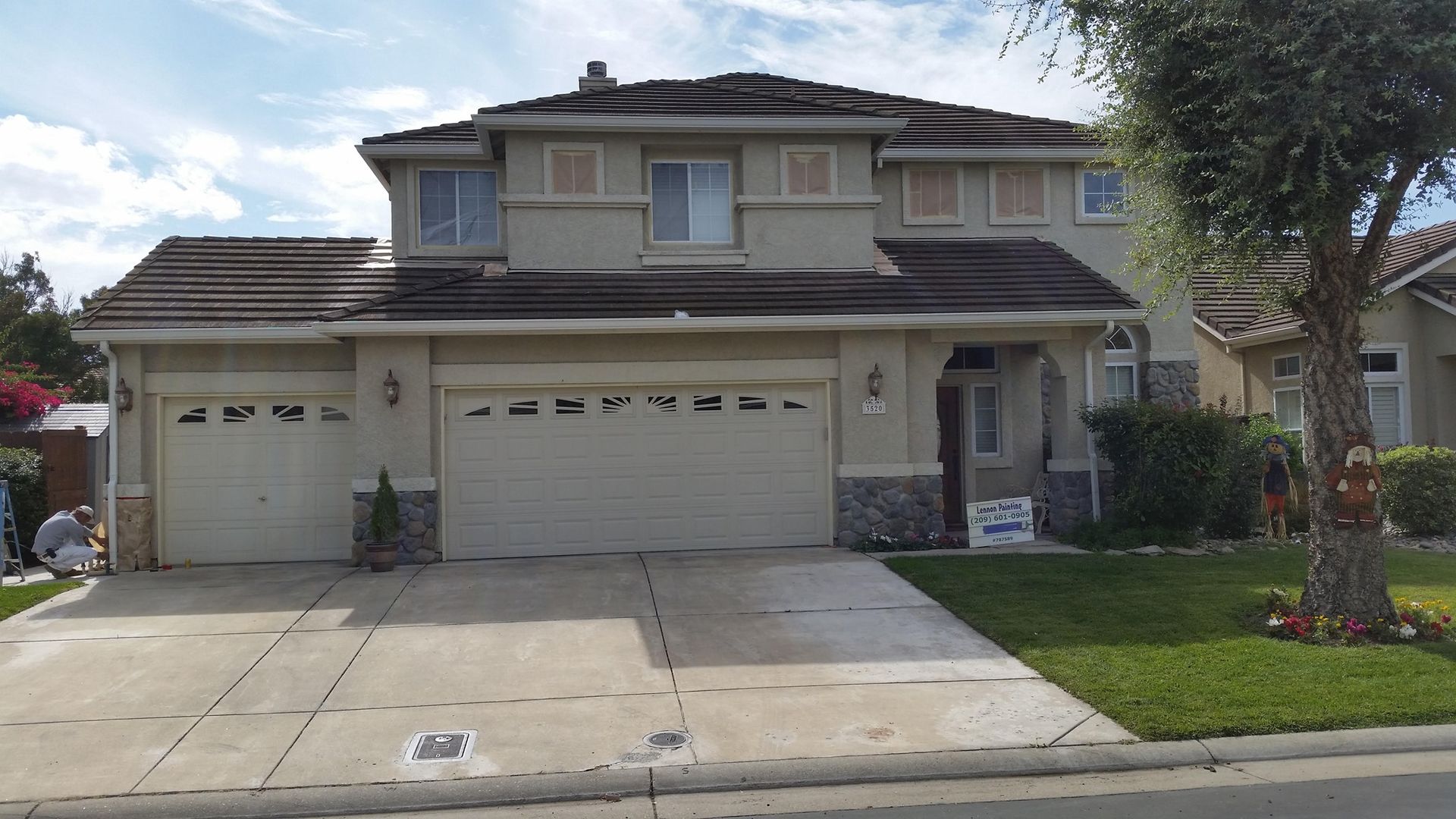 Two-story house with a tan exterior, three-car garage, and a concrete driveway on a sunny day.
