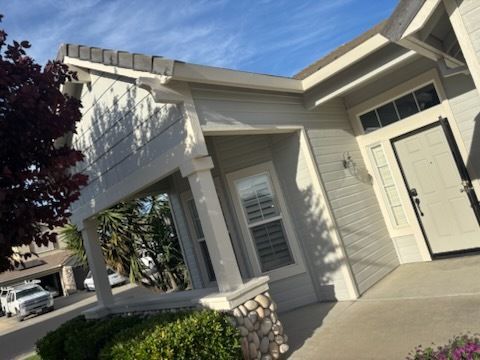Yellow house with black roof, cluttered yard, plants, and blue sky.