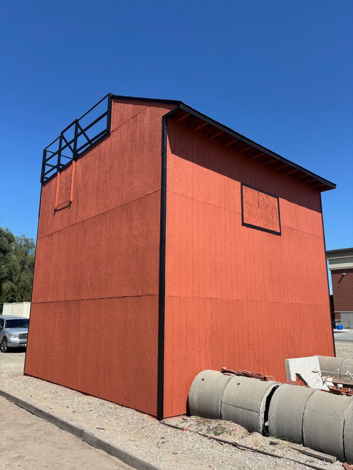 Red wooden tower with black railing and square window, set against a blue sky.