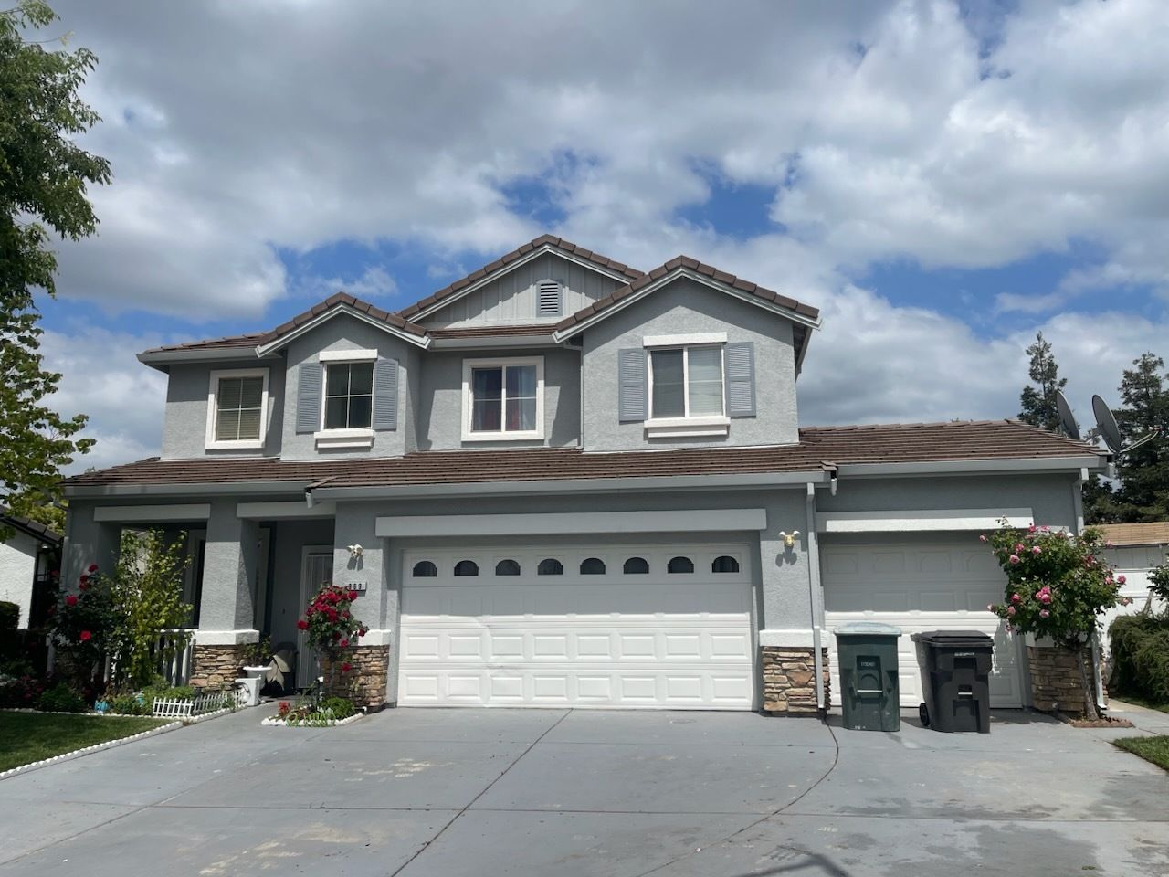 Two-story gray house with white garage doors and blue shutters against a partly cloudy sky.