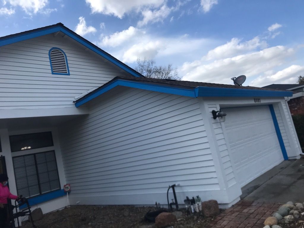 White house with blue trim and a garage door; partially cloudy sky.