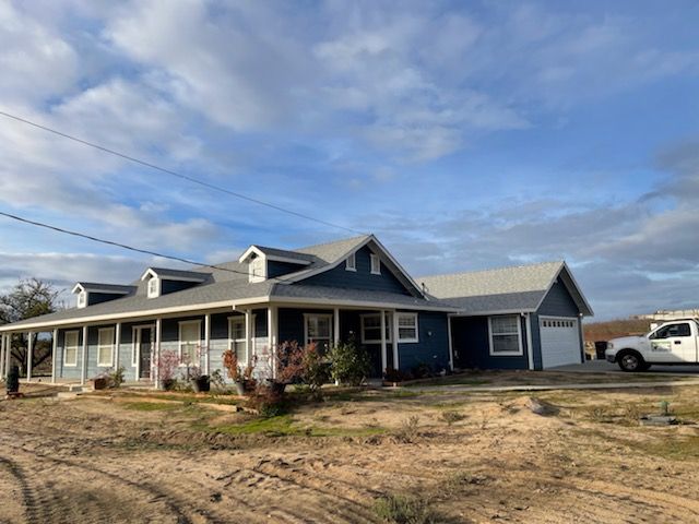 Blue house with a gray roof under a cloudy sky. A white truck is in the background.