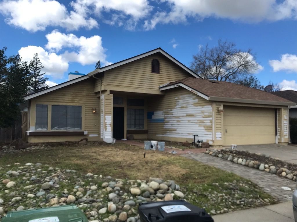 House undergoing exterior work, with peeling paint and masked windows; blue sky background.