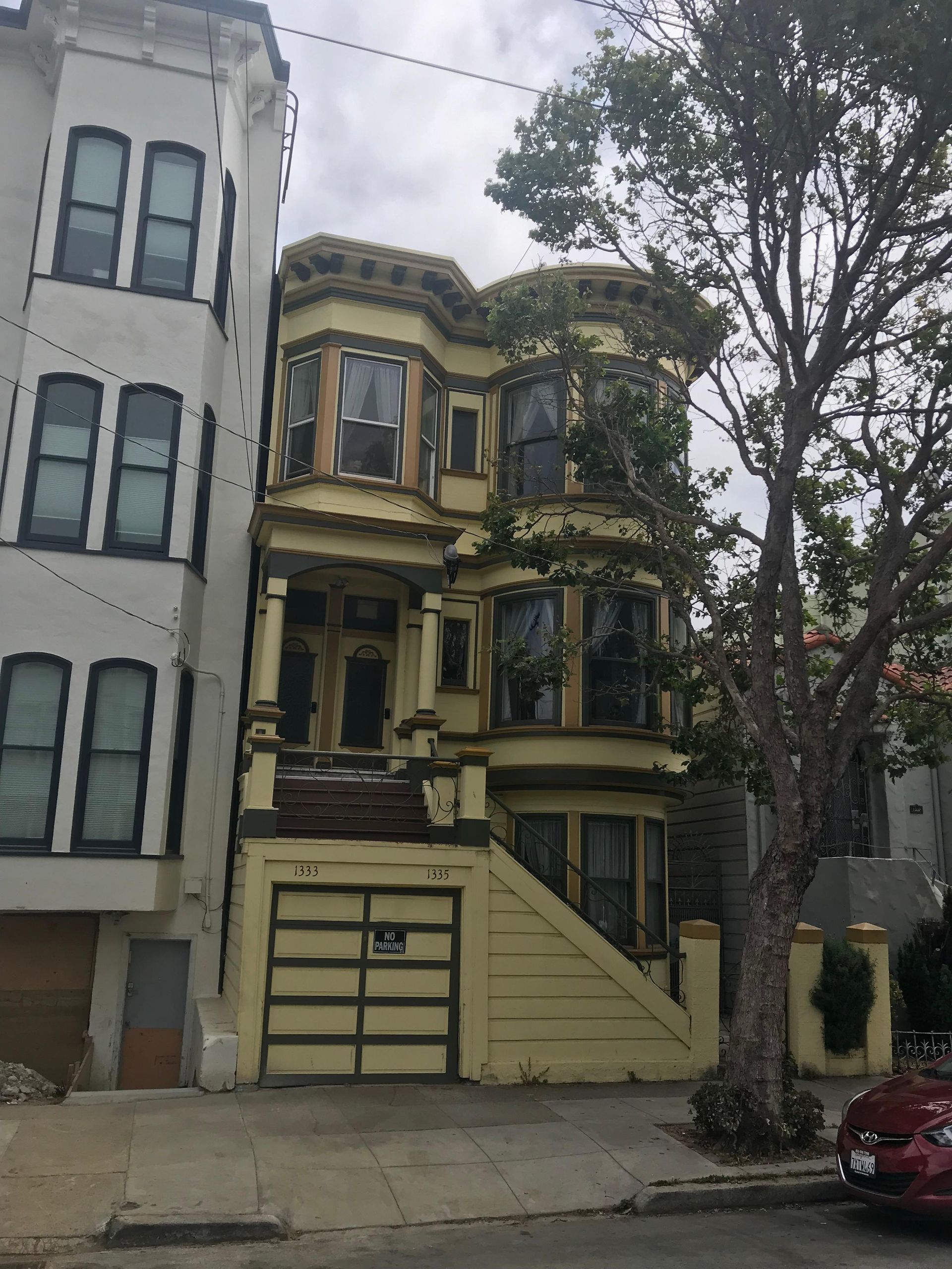 Yellow Victorian house with bay windows, stairs, and a garage in San Francisco.