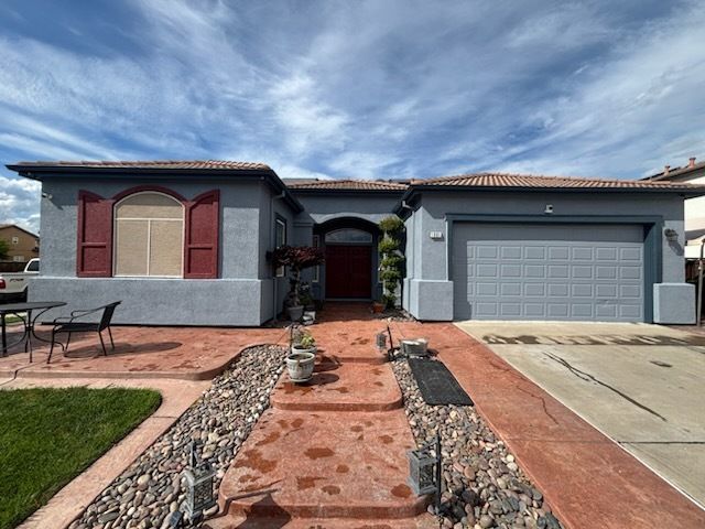 Two-story beige house with a tan garage door, red shutters, and a cloudy sky.