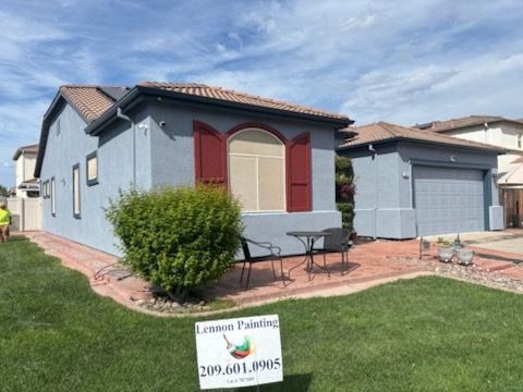 Yellow house with black roof, cluttered yard, plants, and blue sky.