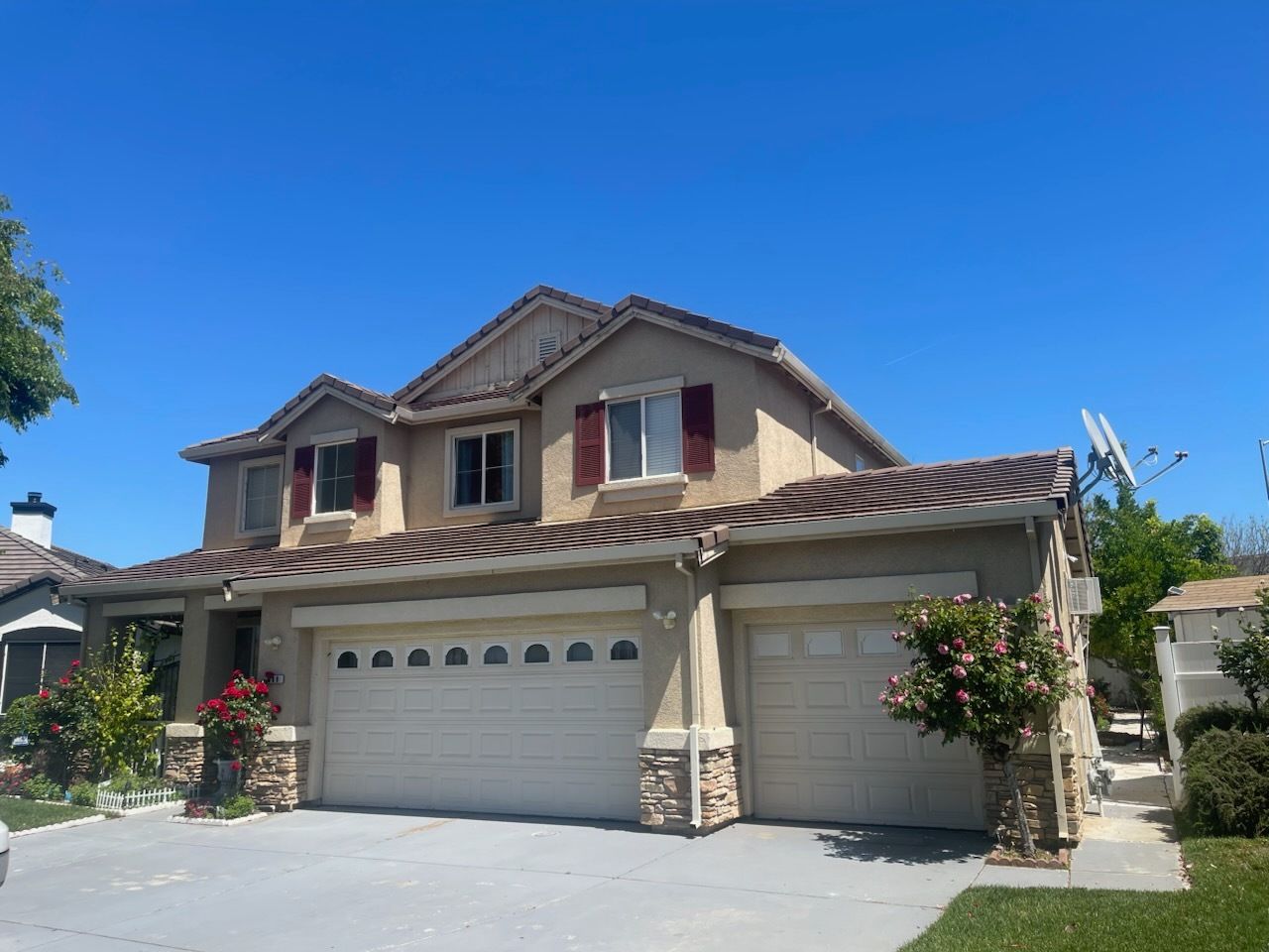 Two-story beige house with a three-car garage, red shutters, and a blue sky background.