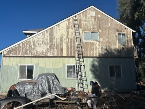 Beige barn-style building with white patches, air conditioning unit, black roof, under a blue sky.