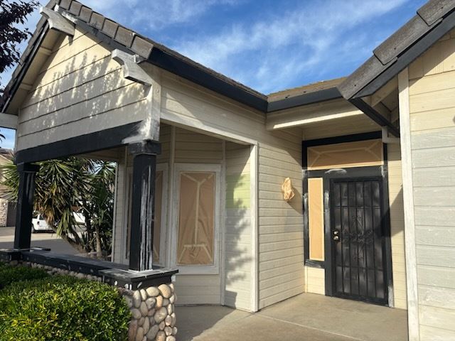 Backyard view of a white house with a dark roof, chimney, and patio. Plants, furniture, and a blue sky are present.