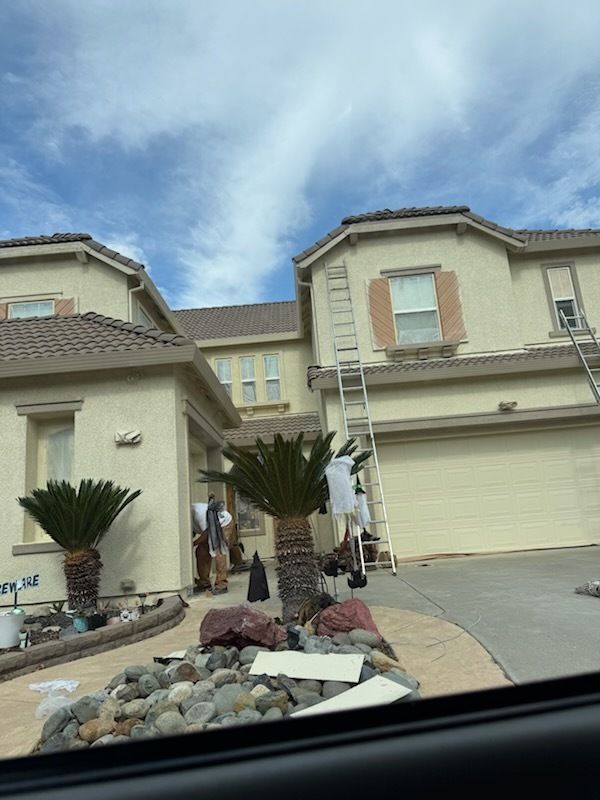 A two-story house with a ladder leaning against it, car in front, cloudy sky.