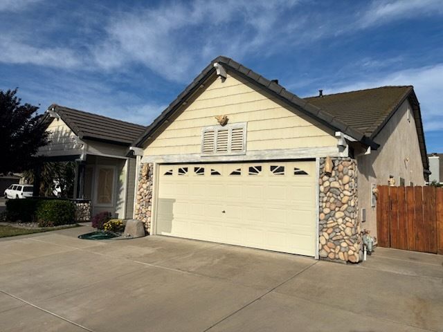 Backyard view of a white house with a dark roof, chimney, and patio. Plants, furniture, and a blue sky are present.