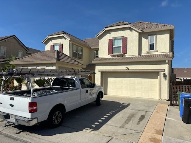 Yellow house with black roof, cluttered yard, plants, and blue sky.