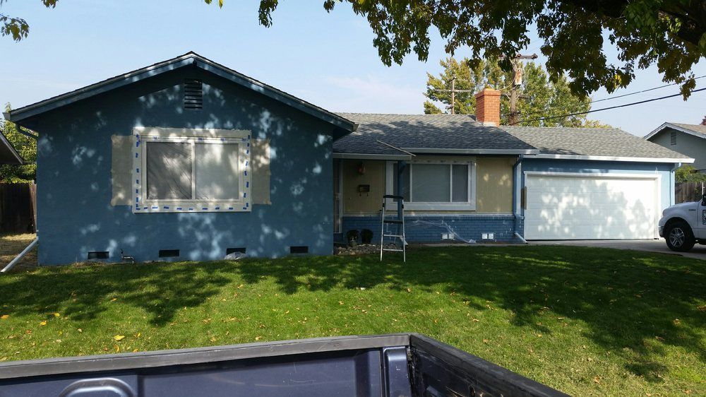 Blue house with white trim; exterior wall under construction; green lawn and clear sky.